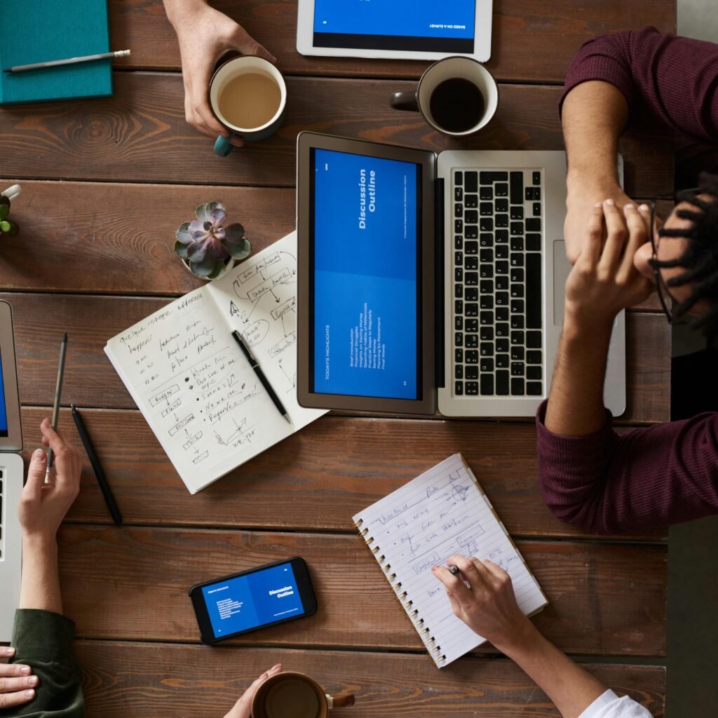 pexels-photo-3183165-3183165 Group of coworkers discussing business strategies with laptops and tablets in a modern office setting.